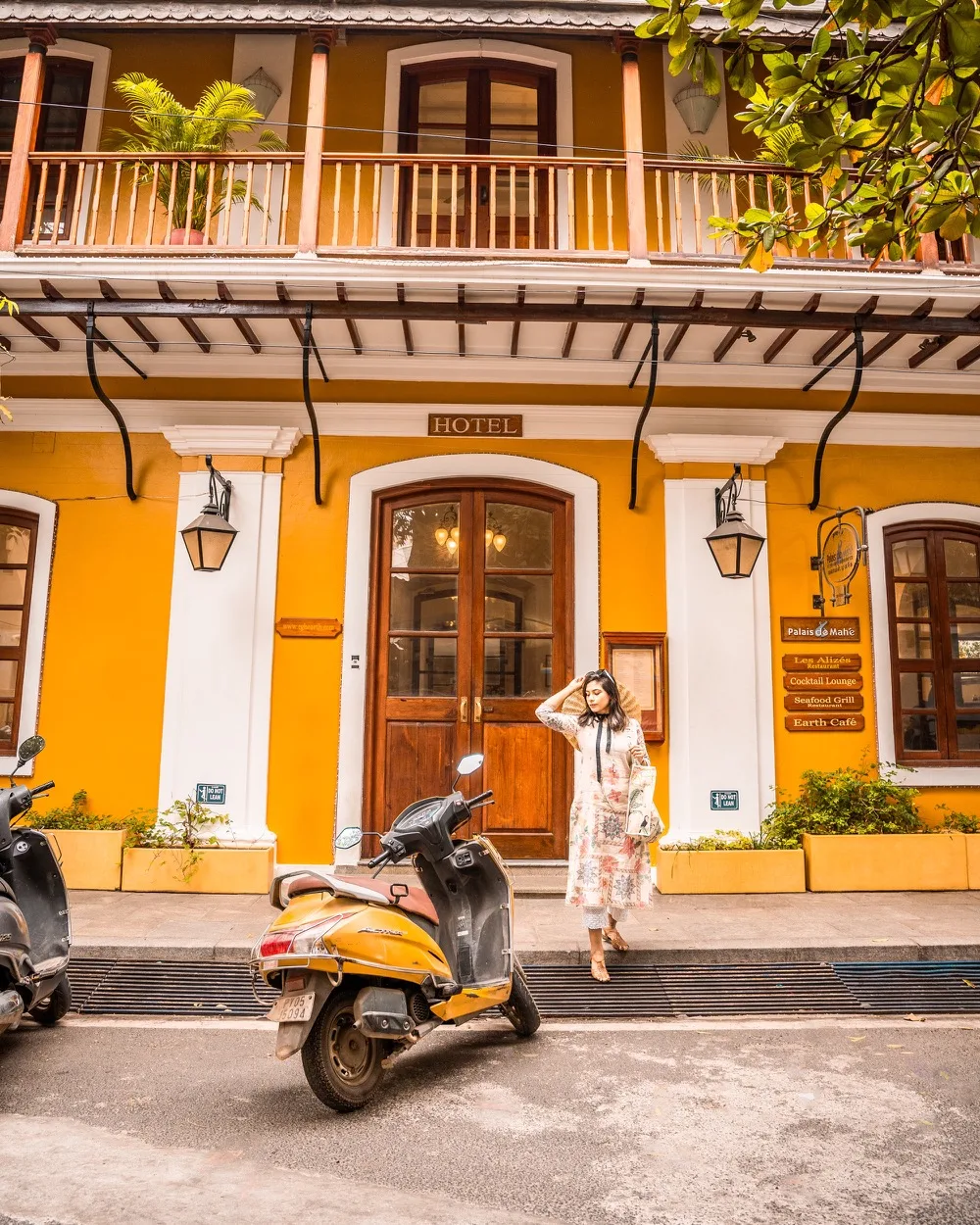 Woman in a sun dress walking past a vibrant mustard-yellow colonial wall with pink bougainvillea in White Town, Pondicherry.