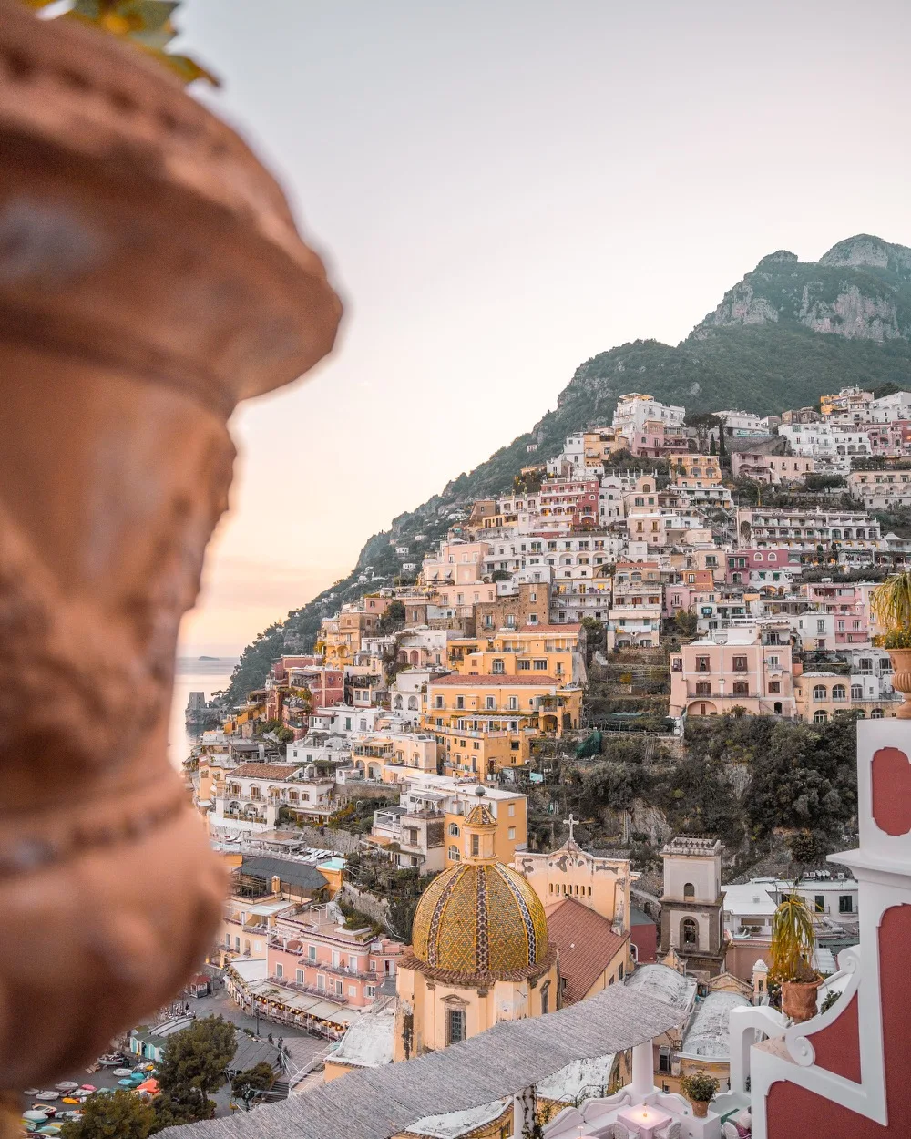 Sunset view over pastel cliffside houses and the tiled dome of Positano on the Amalfi Coast.
