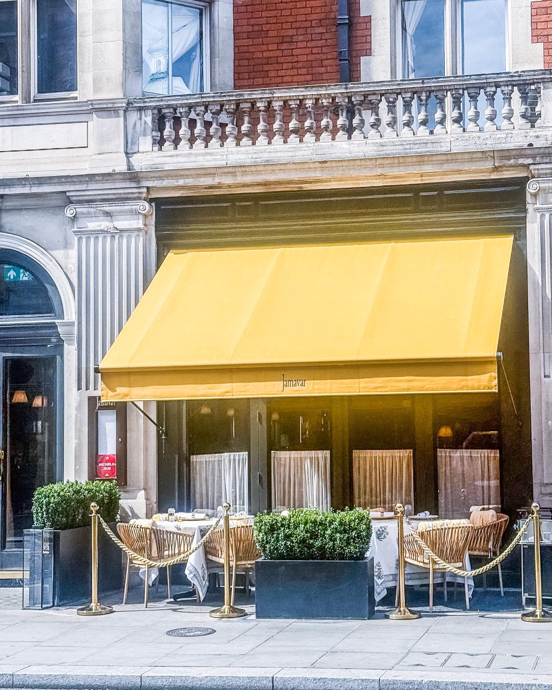 Elegant street-side restaurant terrace with a bright yellow awning and outdoor tables on a historic building façade