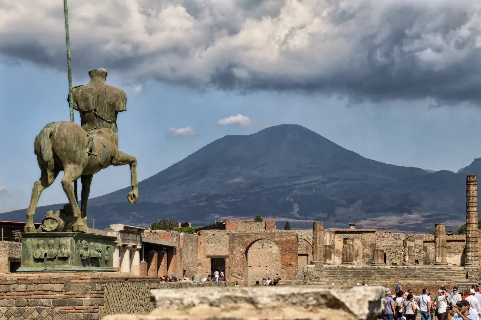 Bronze centaur statue overlooking the ruins of Pompeii with Mount Vesuvius rising under cloudy sky.