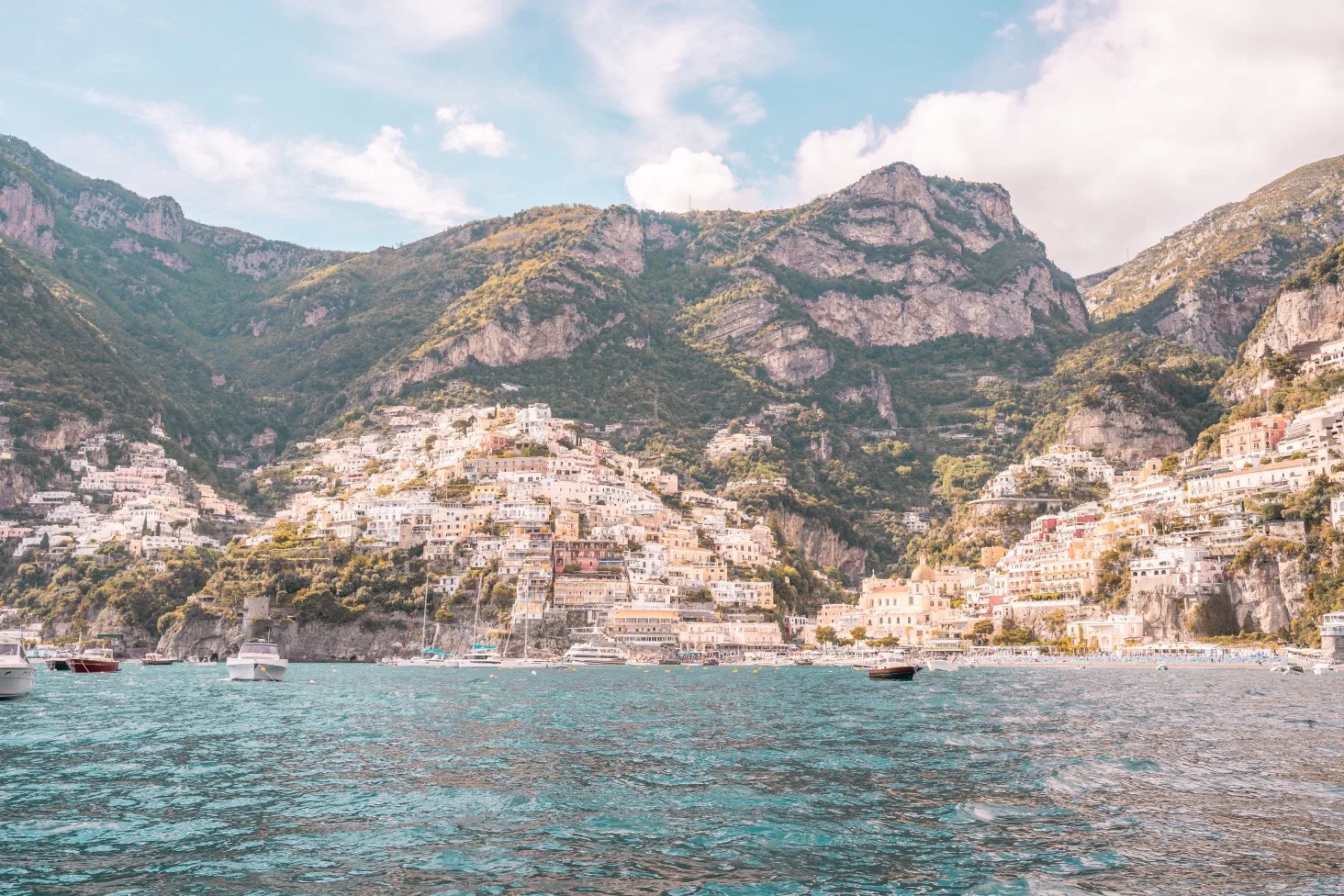 Colourful cliffside village overlooking turquoise sea with boats moored in the bay beneath steep Mediterranean mountains