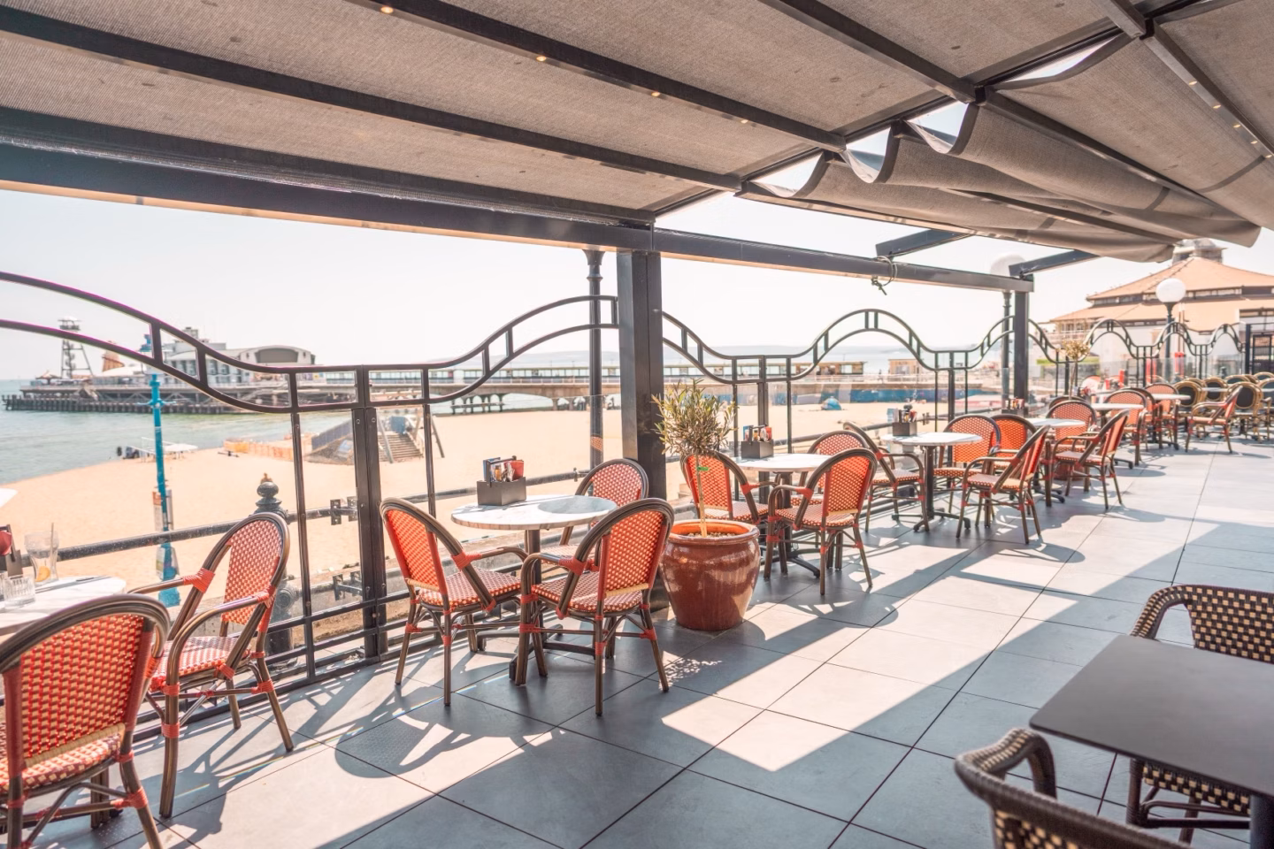 Harry's covered terrace with red bistro chairs overlooking Bournemouth beach and pier