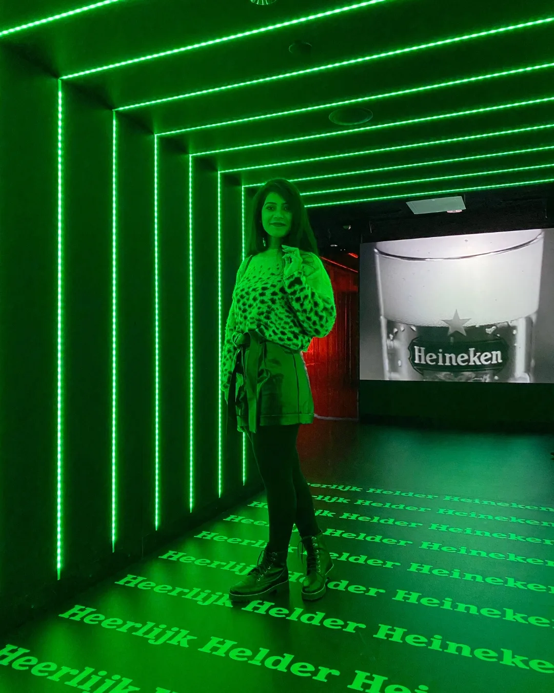 Woman posing in a neon-green lit corridor with Heineken branding projected on the floor and a beer image on the wall.