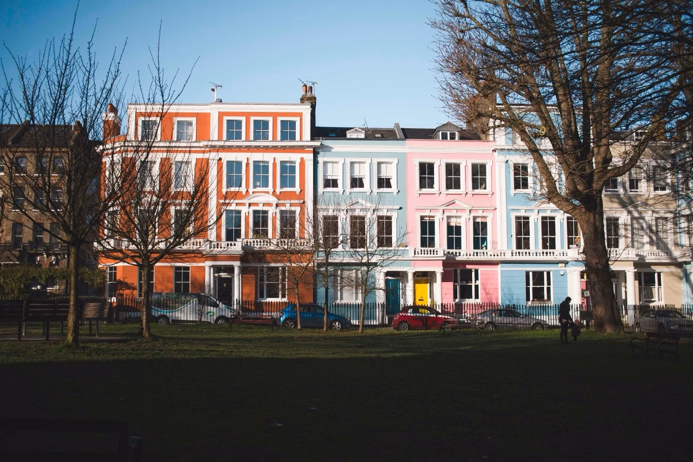 Colourful pastel townhouses across from a park, with leafless trees framing the street scene