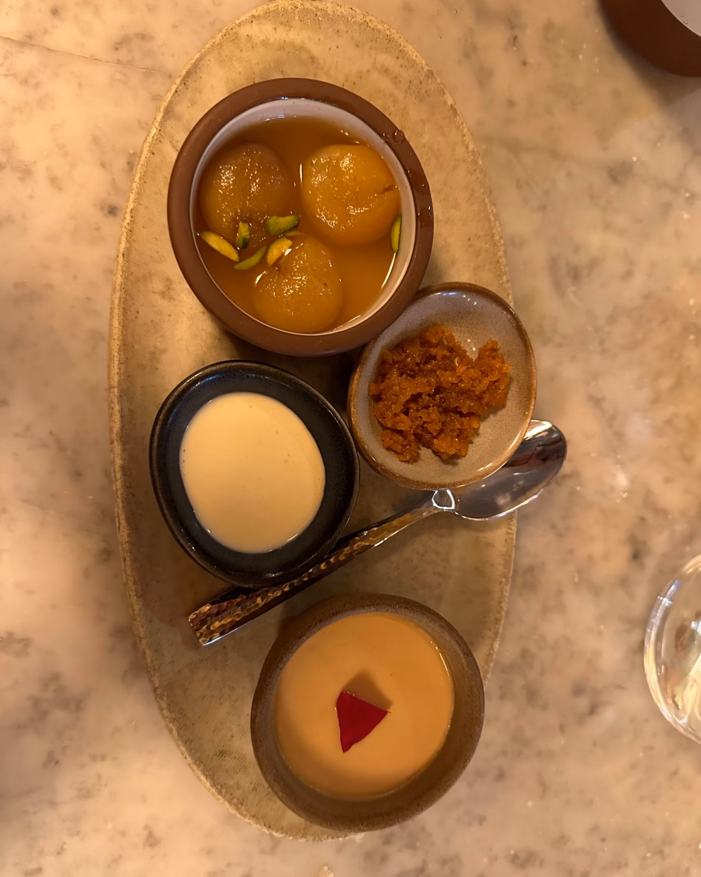 A plated dessert assortment with syrup-soaked dumplings, cream, and garnishes on a marble table